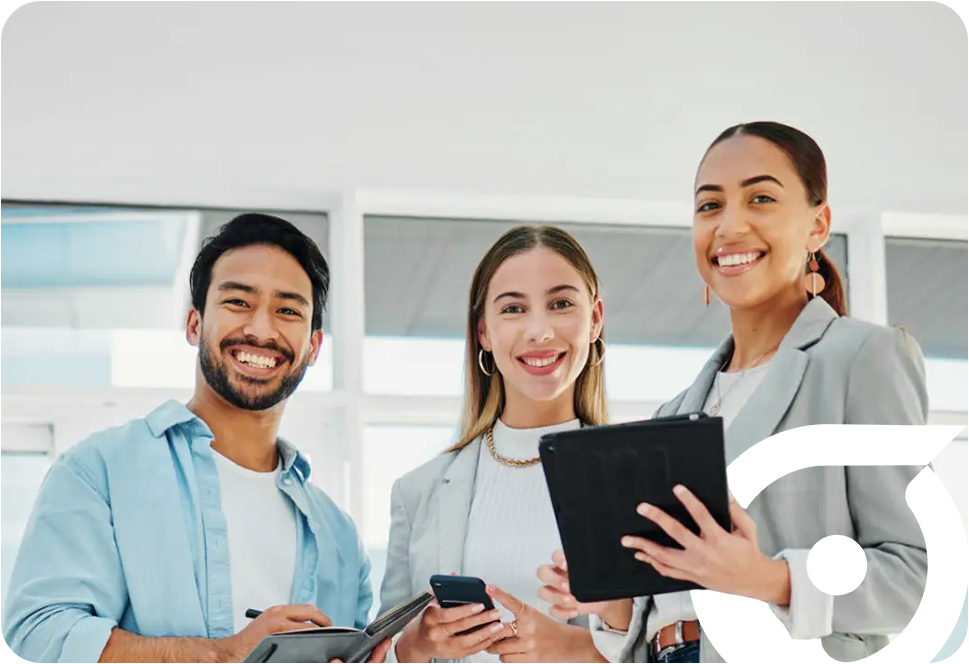 Three smiling professionals hold devices and stand together in a bright indoor setting.