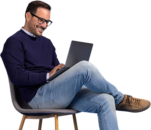 A Man sitting in a chair and working on a laptop, appearing focused and relaxed.
